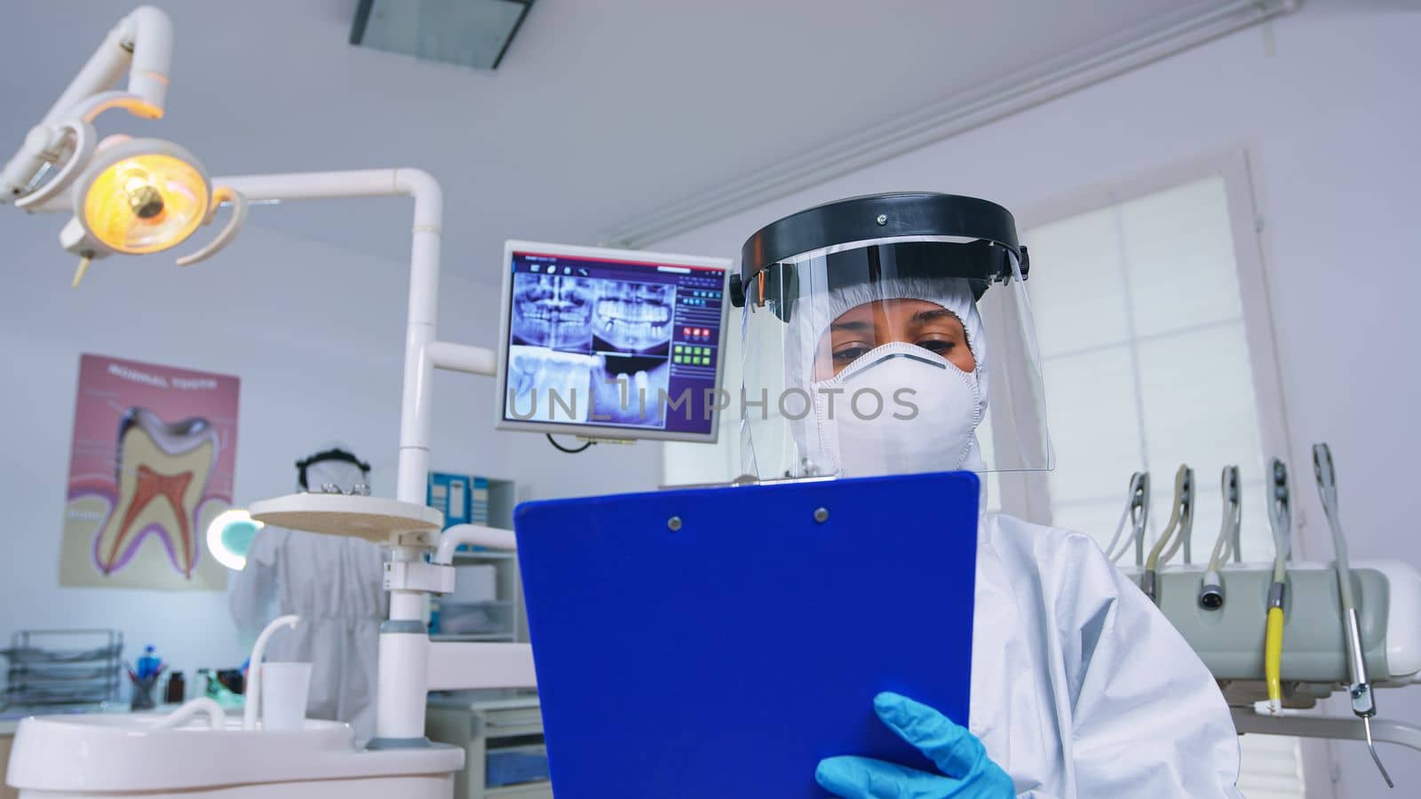 Pov of patient getting dental treatment in dentist office with new normal, doctor taking notes on clipboard before examining. Stomatolog wearing safety gear against coronavirus during heatlhcare check