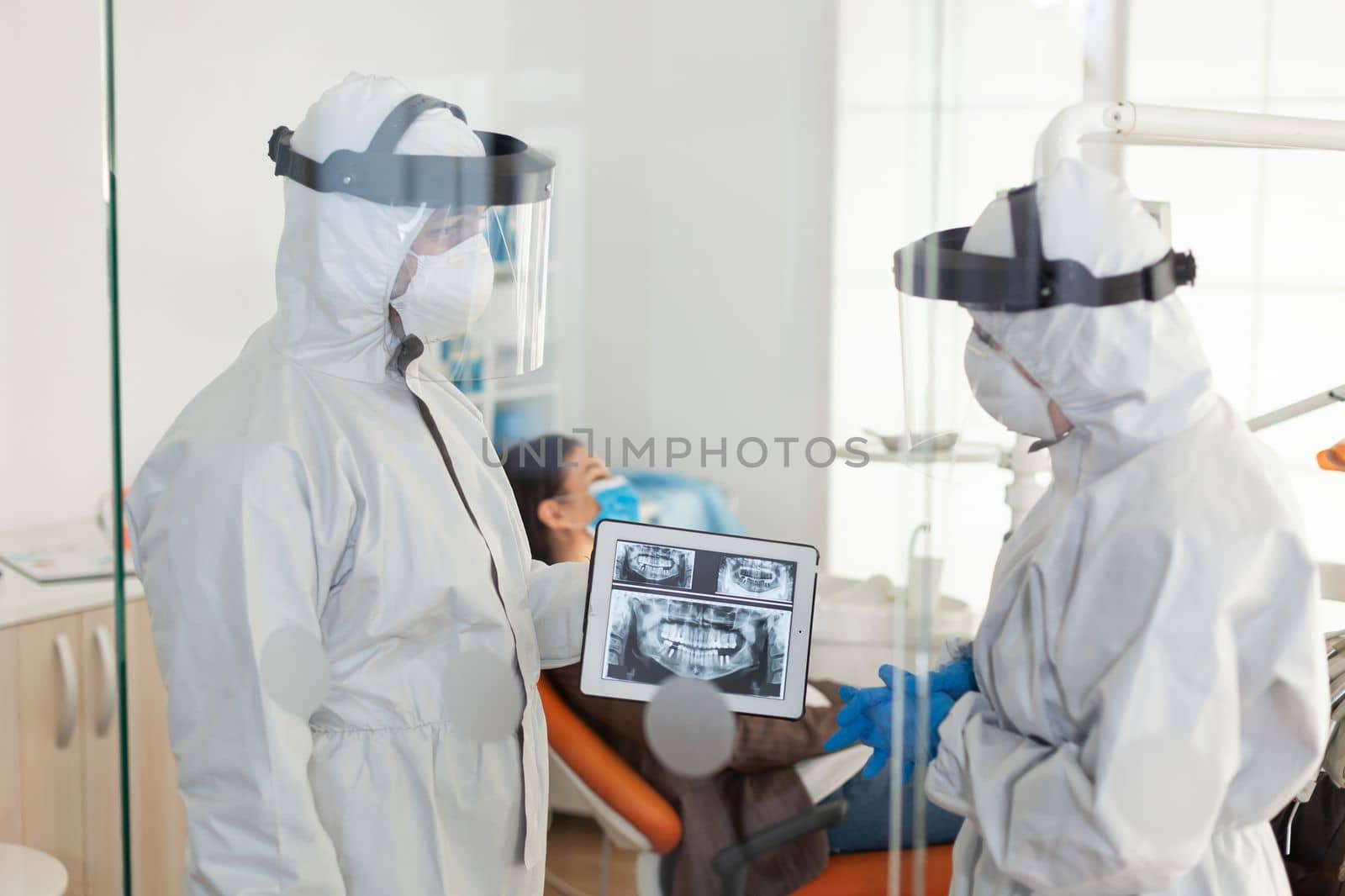 Dentist doctors with ppe suit analysing teeth x-ray using tablet by DCStudio