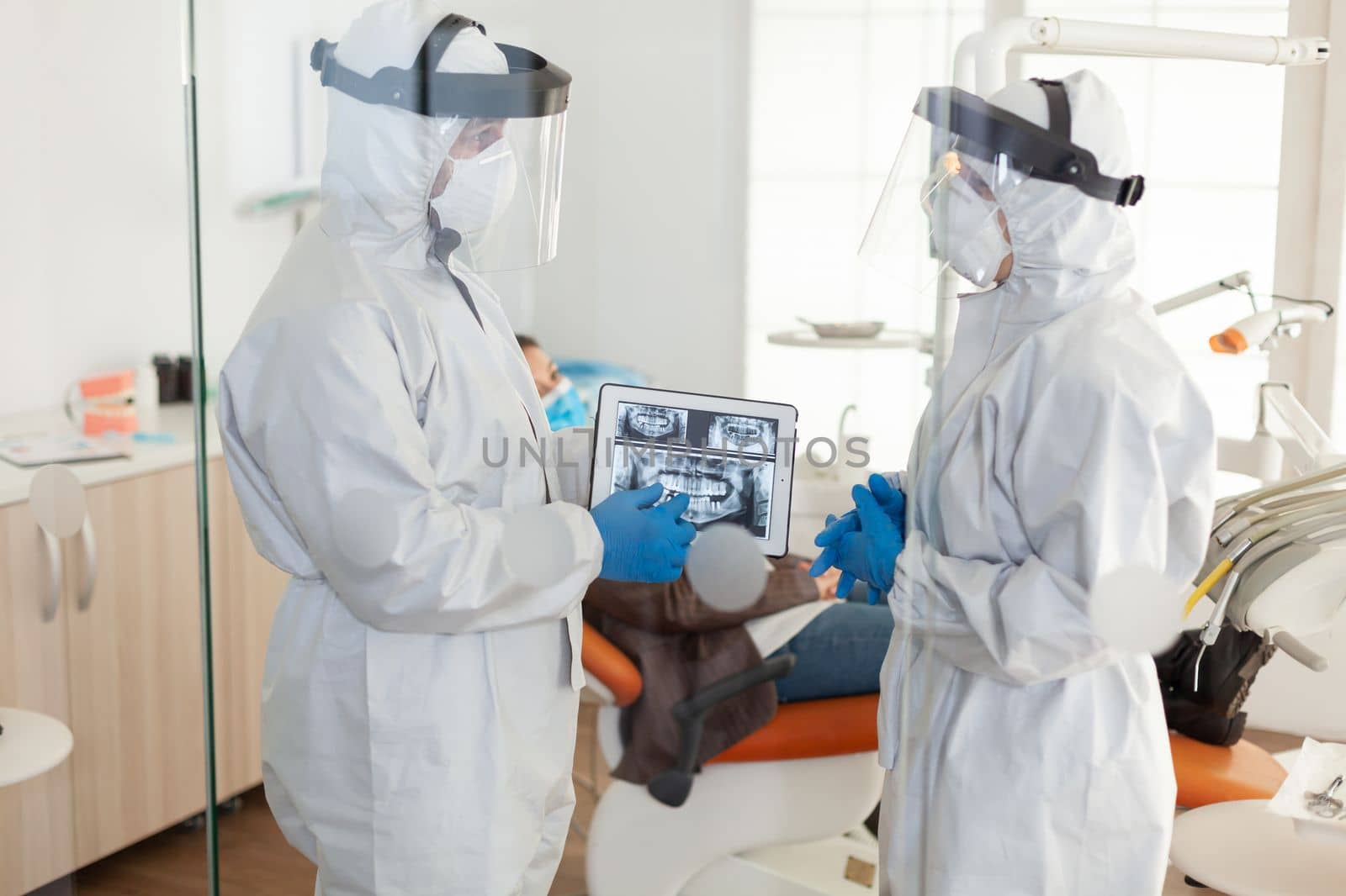 Dentist doctors with ppe suit analysing teeth x-ray using tablet by DCStudio