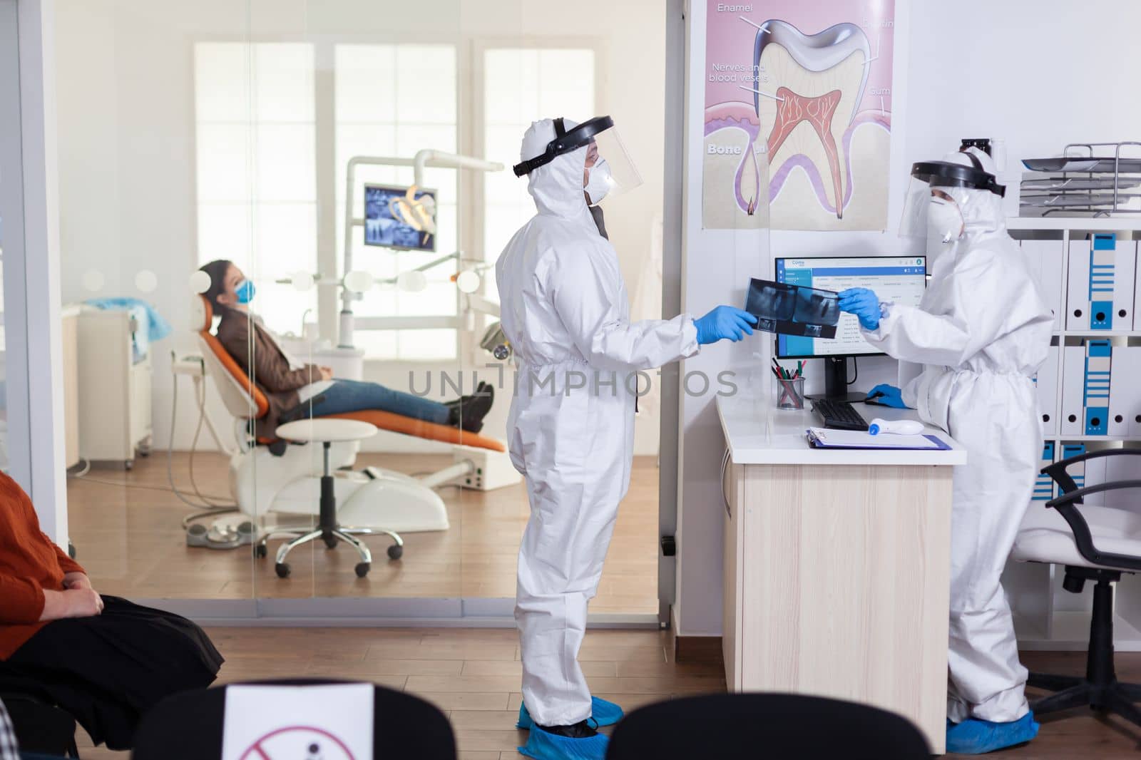 Dental receptionist dressed in coverall giving doctor patient x-ray by DCStudio