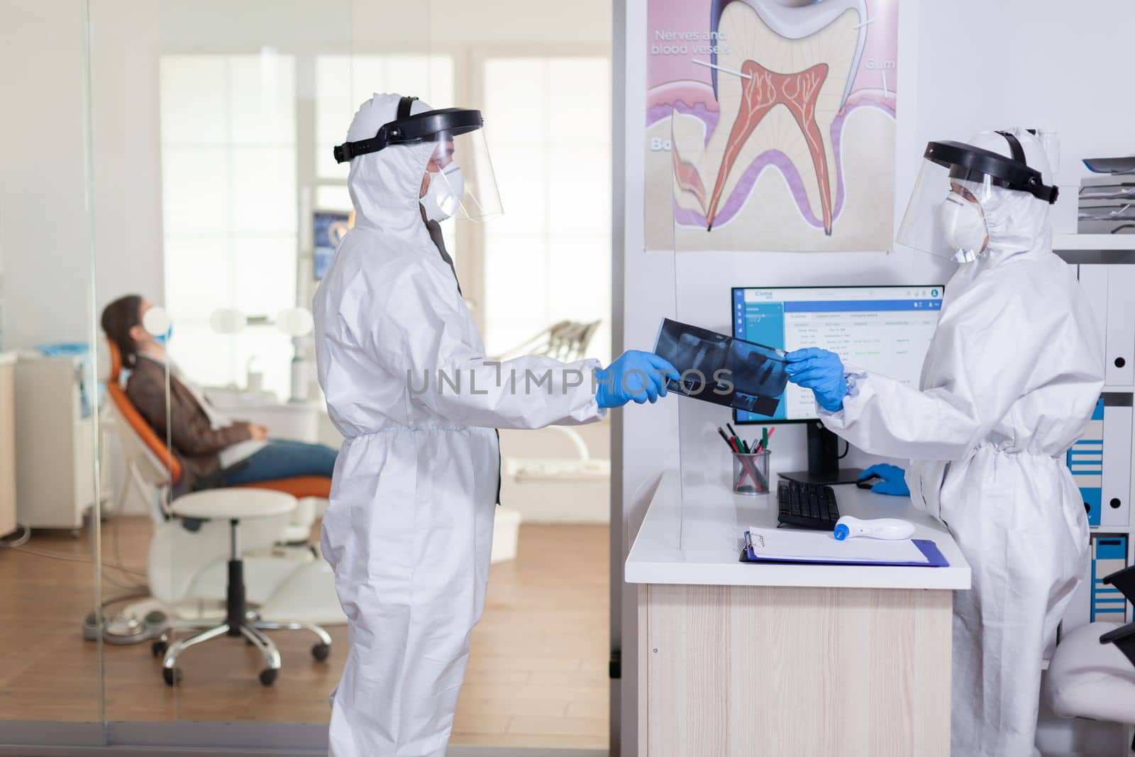 Dental receptionist dressed in coverall giving doctor patient x-ray by DCStudio
