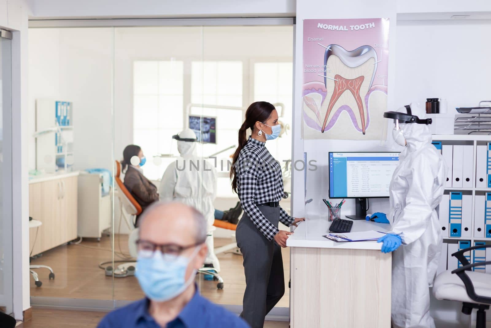 Dentist nurse dressed in ppe suit with face shiled discussing with patient by DCStudio