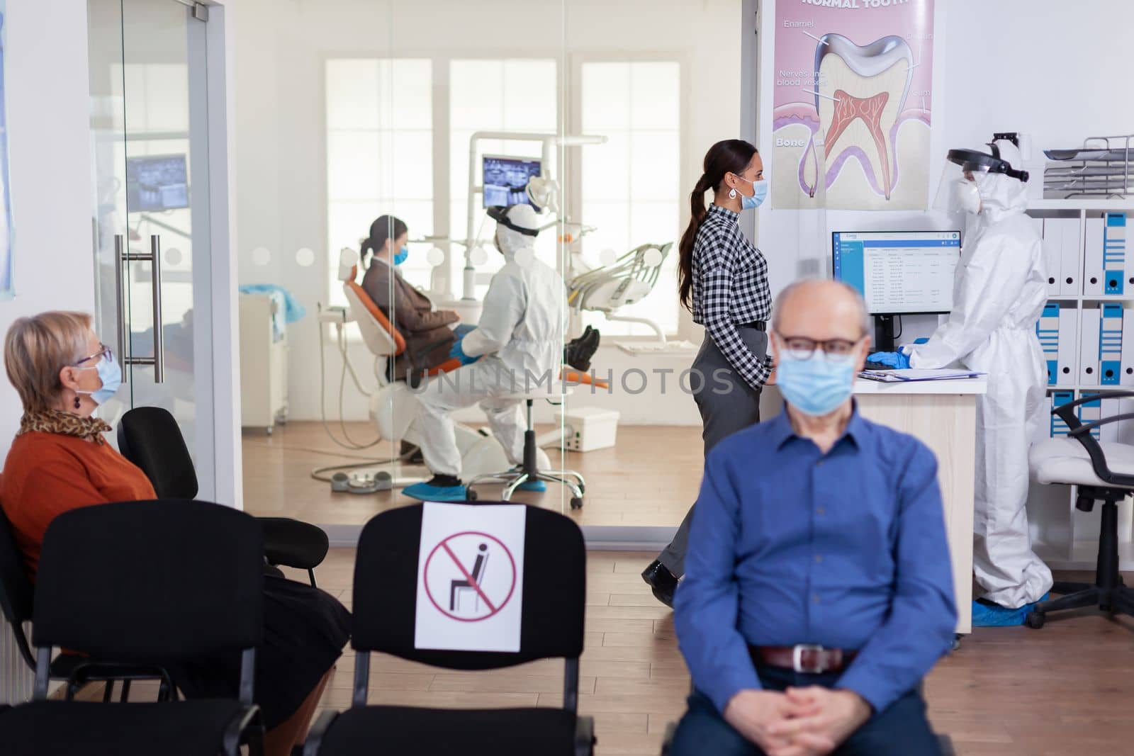 Dentist nurse dressed in ppe suit with face shiled discussing with patient by DCStudio