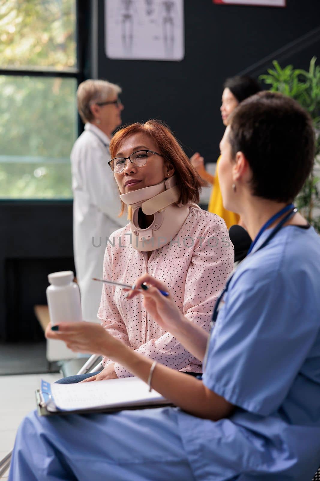 Senior patient with cervical neck collar having medical appointment in hospital waiting area. Specialist holding pills bottles explaining medication prescription. Medicine support