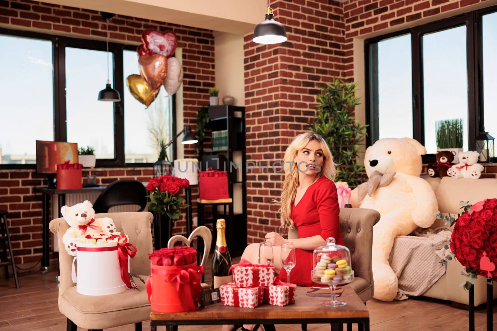 Attractive woman sitting in living room filled with romantic gift, enjoying celebrating love holiday. Cute sexy girlfriend in red dress receiving valentine s day presents from boyfriend