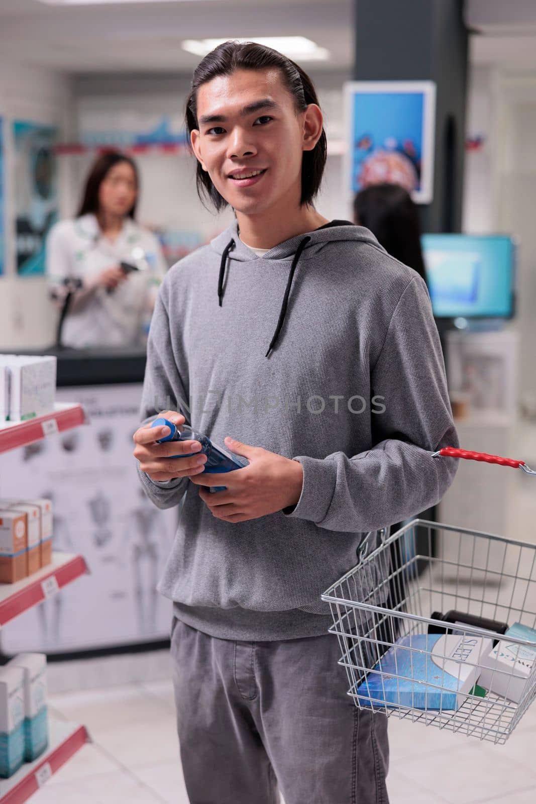 Asian young adult coming at pharmacy shop to buy medication and prescription treatment, looking at boxes of health care products on shelves. Customer holding pharmaceutical supplies in drugstore.