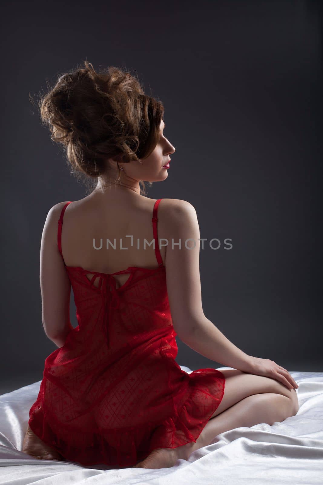 Sexy woman in red lingerie on white silk bed look at light