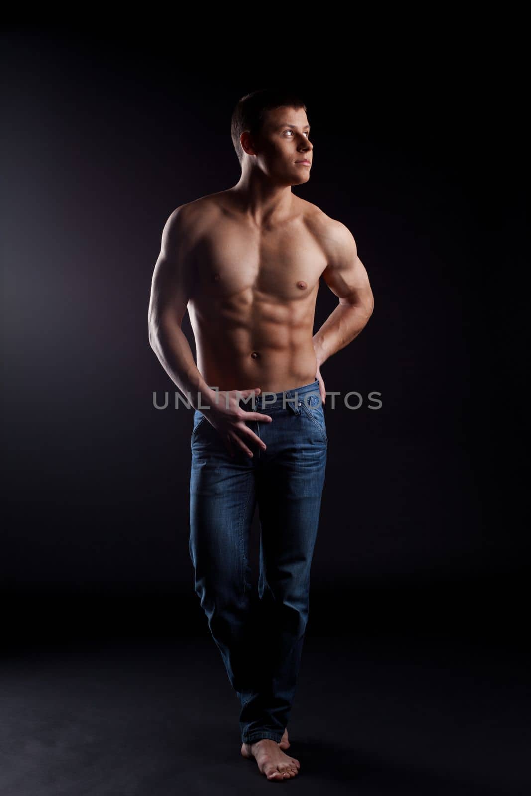 youn strong man with naked torso in jeans posing in dark