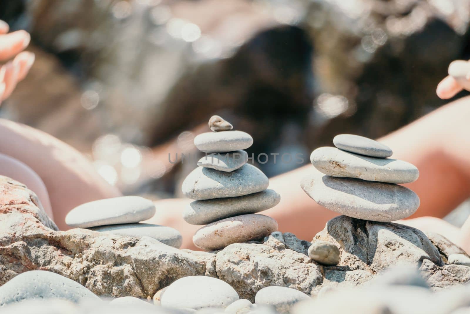 Woman with daughter bilds stones pyramid on seashore on a sunny day on the blue sea background. Happy family holidays. Pebble beach, calm sea. Concept of happy vacation on the sea, meditation, spa by panophotograph