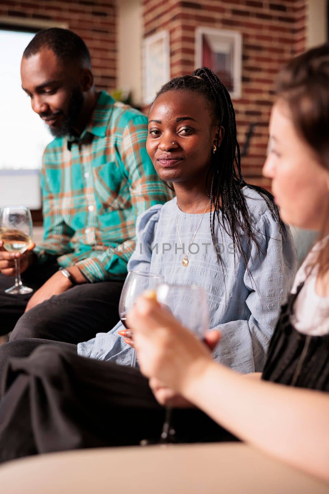 Happily smiling young adult african american woman vertical close up shot enjoying social life, drinking wine at mates, partners apartment, home, house made party, reunion, gathering.