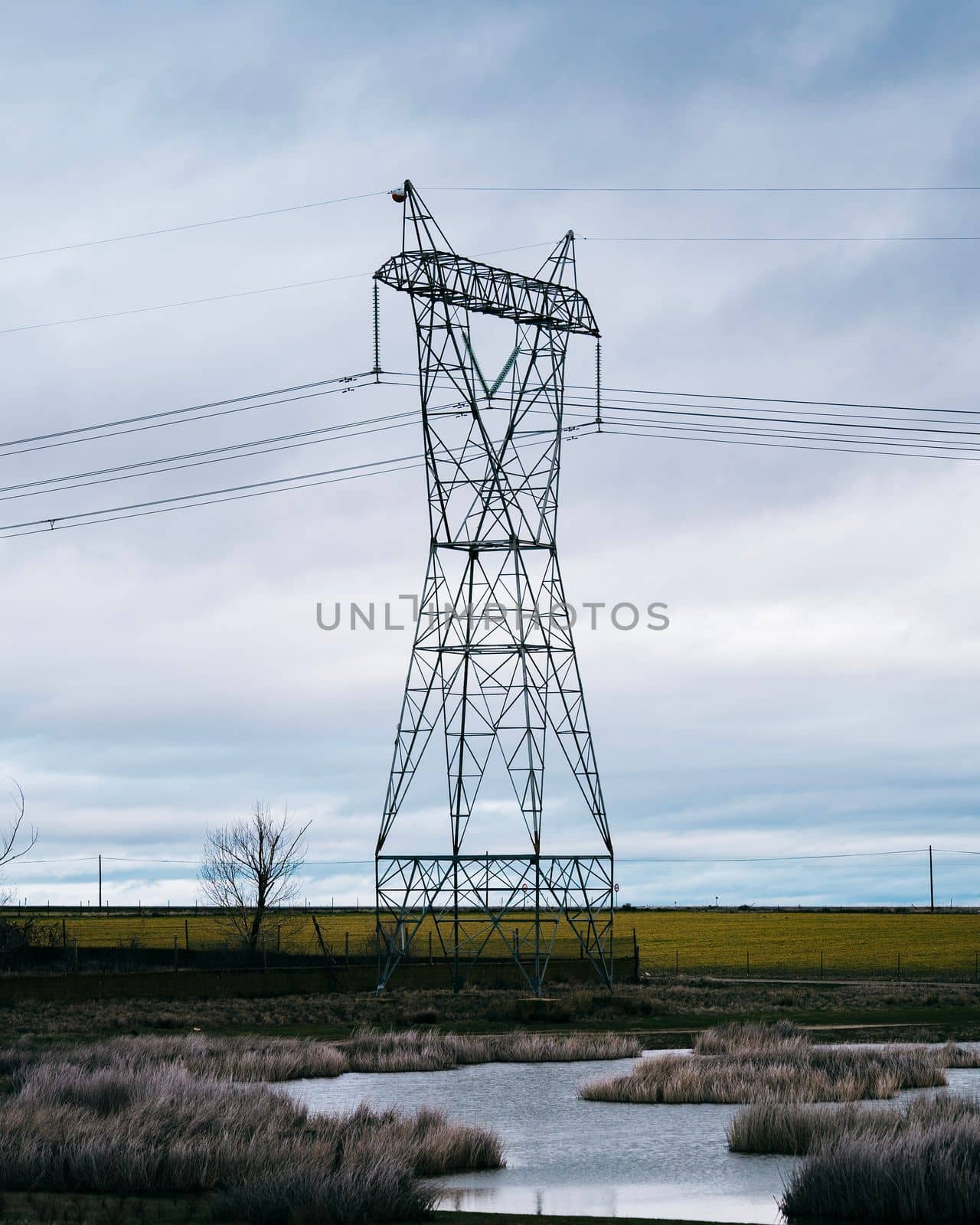 High voltage post or High voltage tower in the countryside with a small lake. Cloudy background by papatonic