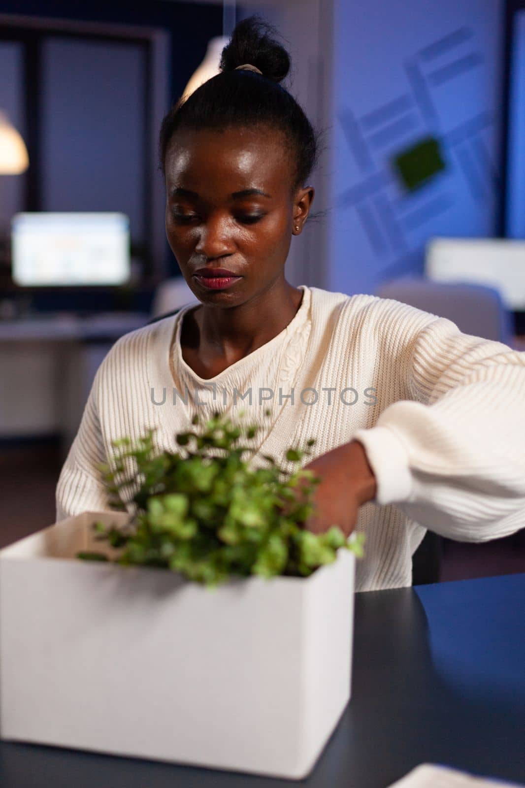 Relocated african american businesswoman putting objects in cardboard box after is fired late at night in startup company office. Resigned tired entrepreneur woman leaving communication job