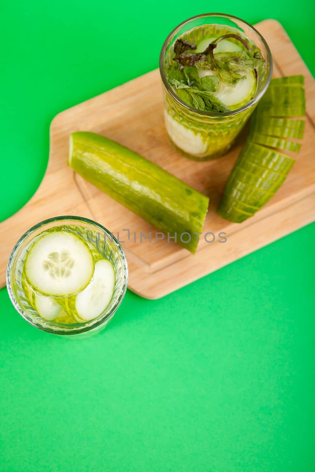 Homemade detox water from organic cucumbers in a glass against a green background