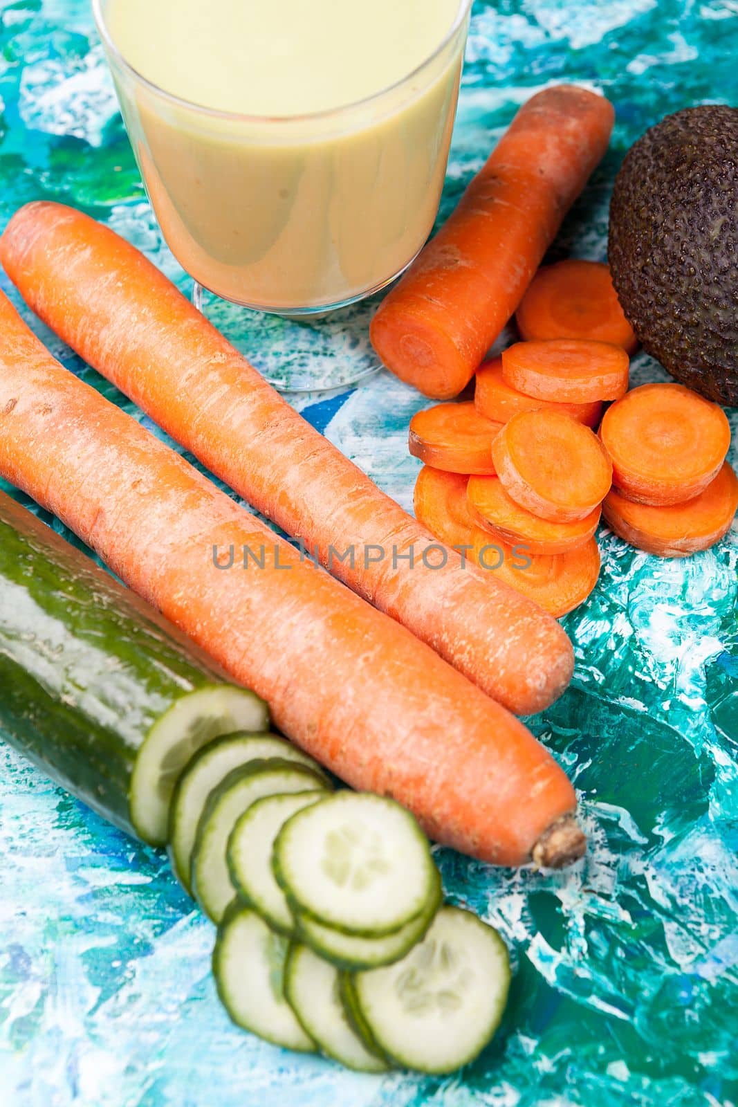 Cucumber, carrots and avocado next to a healthy green smoothie by DCStudio
