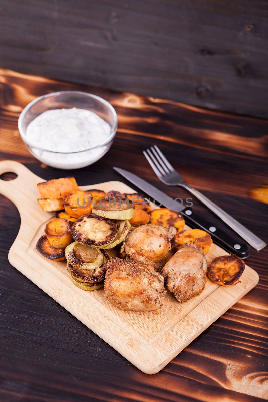 Grilled chicken next to fried zucchini and sweet potatoes on wooden background
