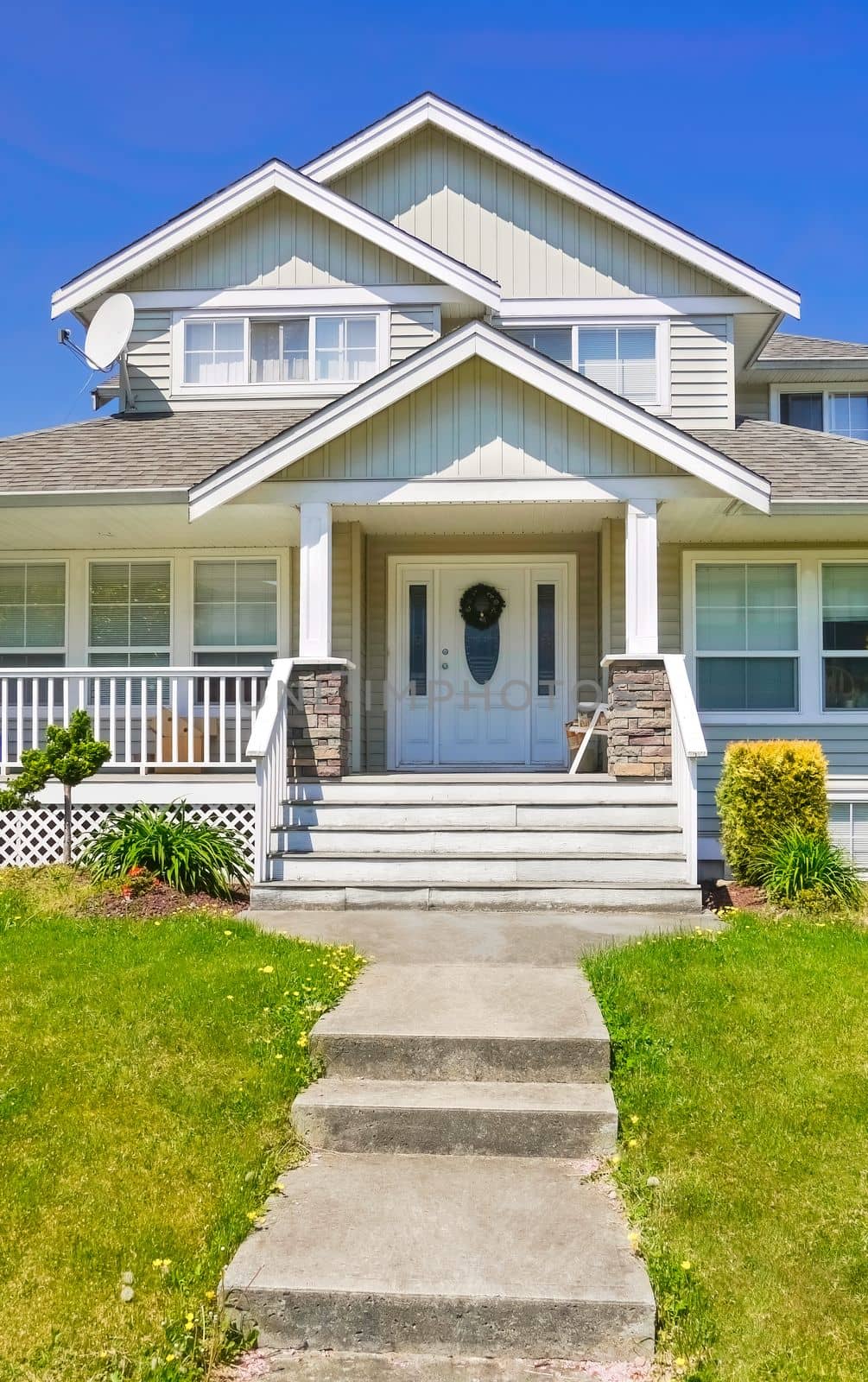Entrance of family house with concrete pathway over green lawn in front.