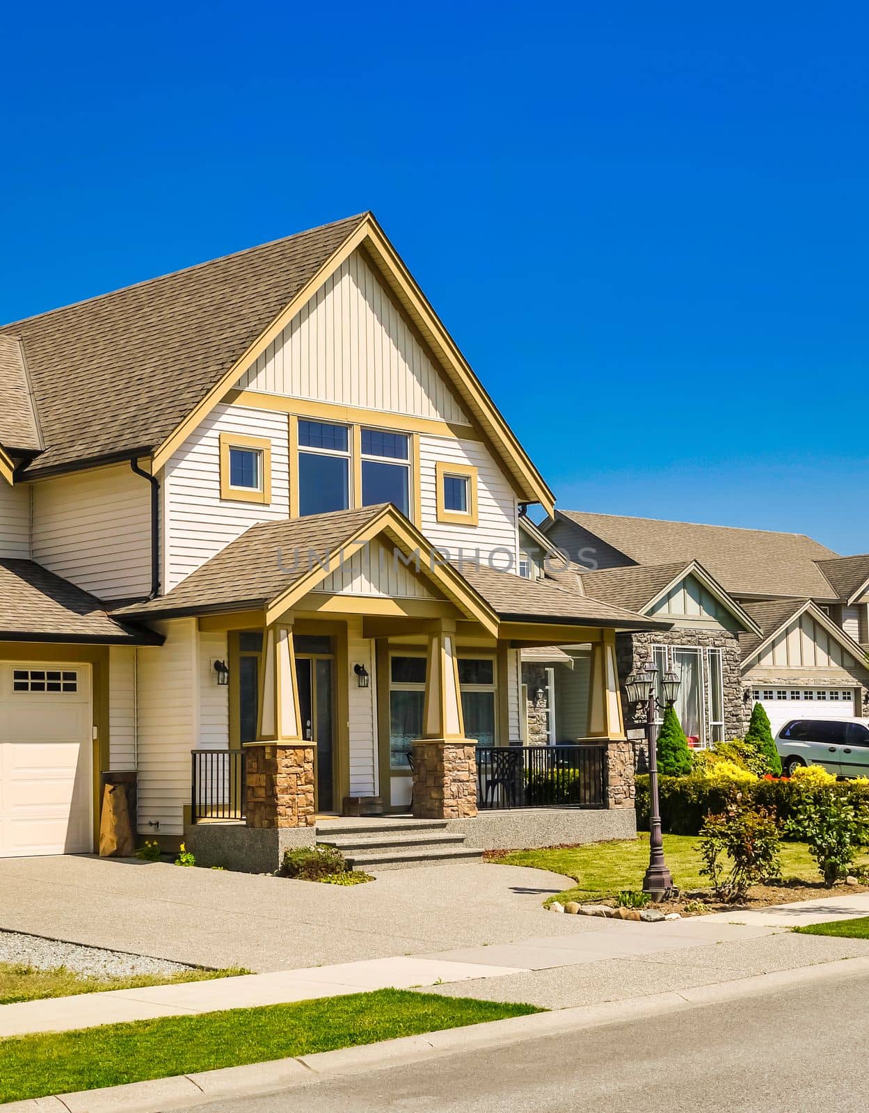 A perfect neighborhood. Big family house with concrete driveway to the garage. Residential house with door steps and porch over entrance on blue sky background