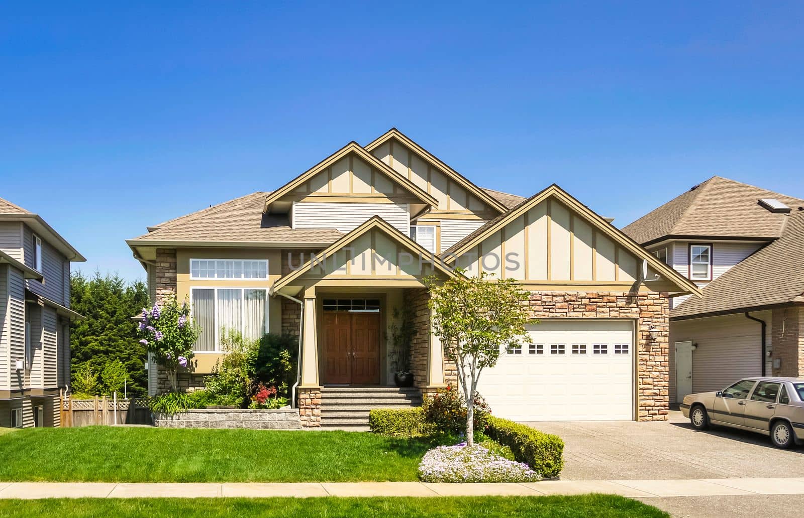 A perfect neighborhood. Luxury family house with car parked on concrete driveway. Residential house with landscaped front yard on blue sky background