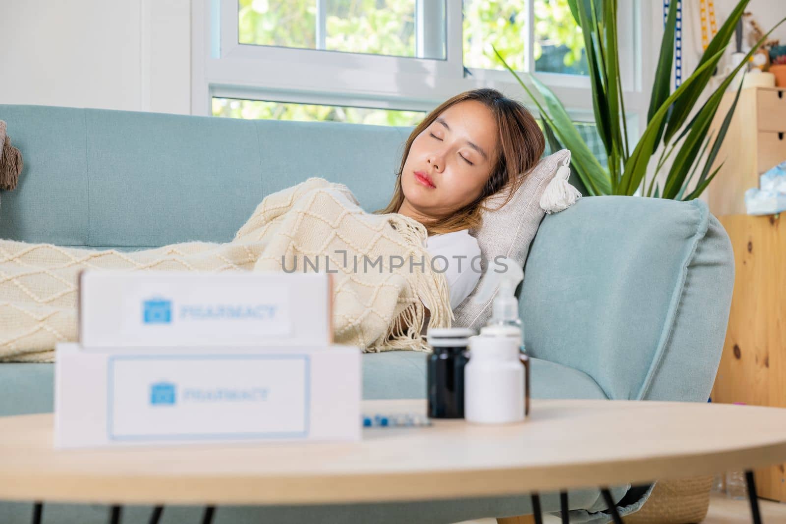 Asian young woman cold sick she sleeping and resting on sofa after take pills at home, beautiful female health problem use pharmacy kit box delivery service from hospital, delivery pharmacy concept