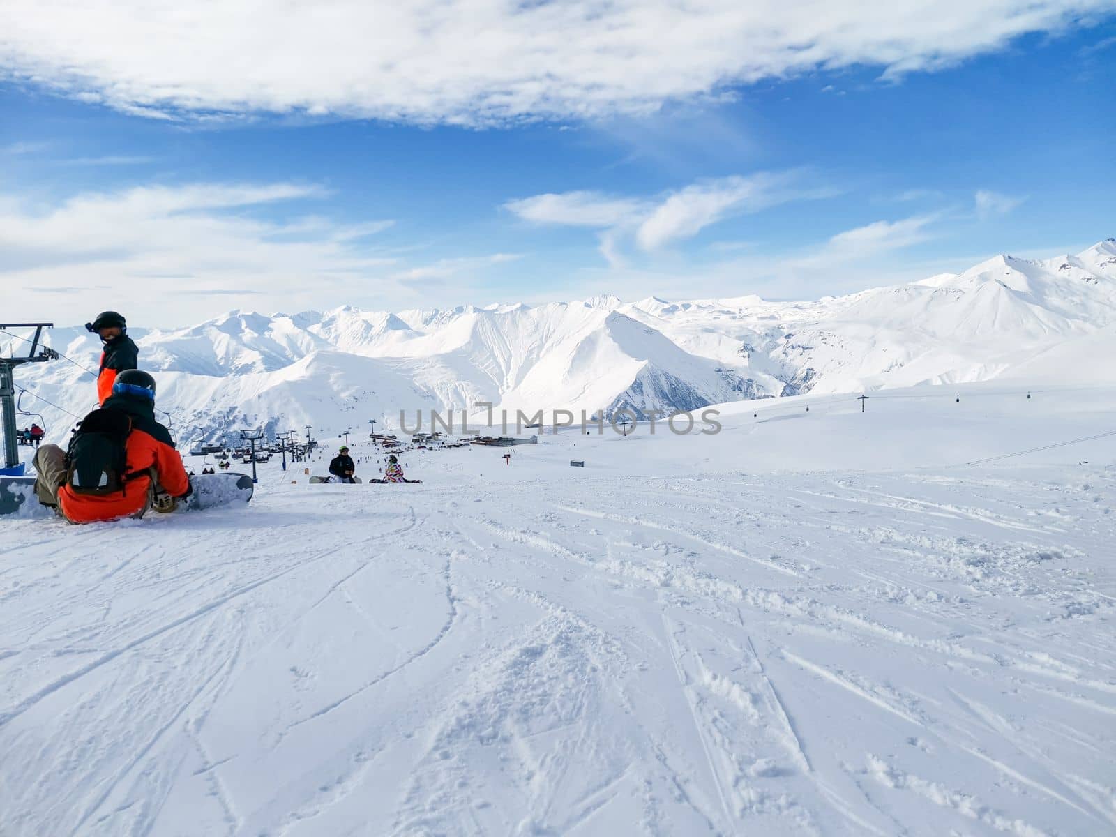 Ski slope. Snowboarder sits on snow. Winter sport. Ski resort of Georgia Gudauri. Snowy slope and mountains