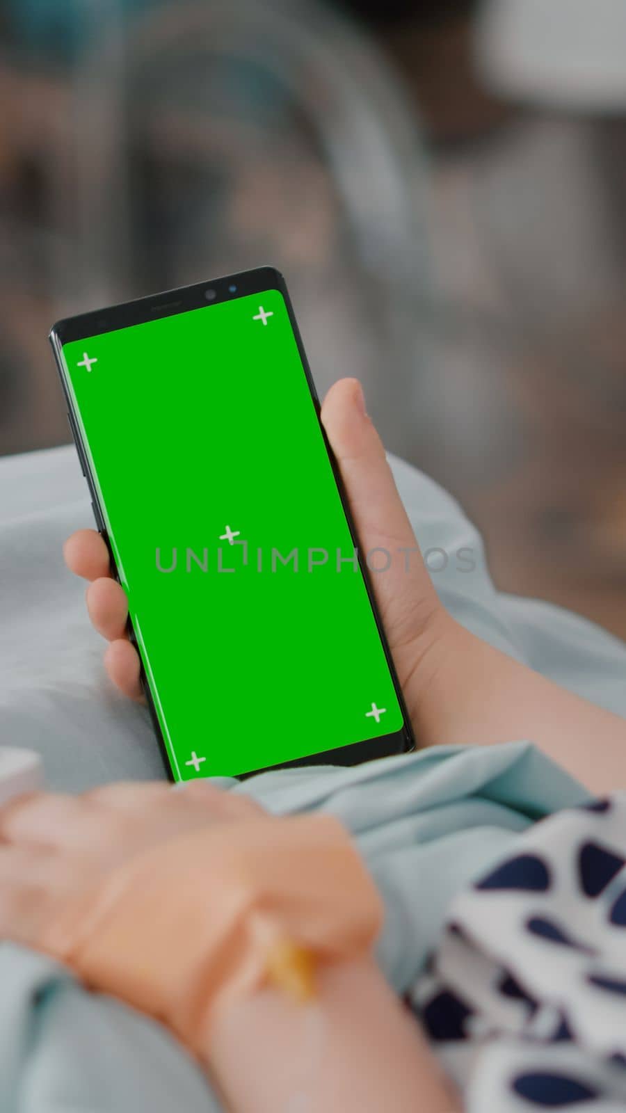 Sick girl holding mock up green screen chroma key phone with isolated display during recovery consultation in hospital ward. Child with oximeter on finger resting in bed after suffering medical surgery