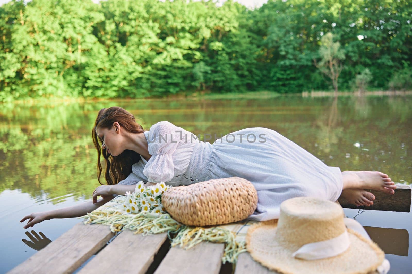 a sophisticated woman in a light dress touches the water while relaxing by the lake by Vichizh