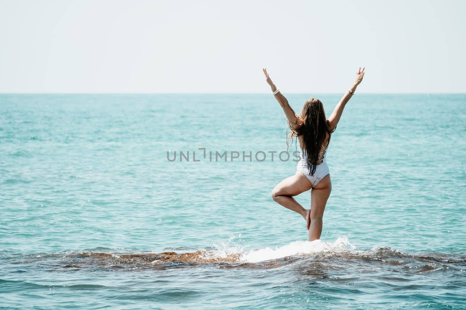 Young woman in swimsuit with long hair practicing stretching outdoors on yoga mat by the sea on a sunny day. Women's yoga fitness pilates routine. Healthy lifestyle, harmony and meditation concept.