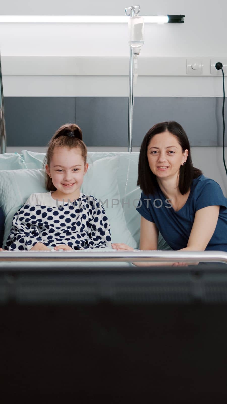 Family watching entertainment cartoon movie on television in hospital ward while waiting for medical expertise during recovery examination. Sick child patient resting in bed after illness surgery