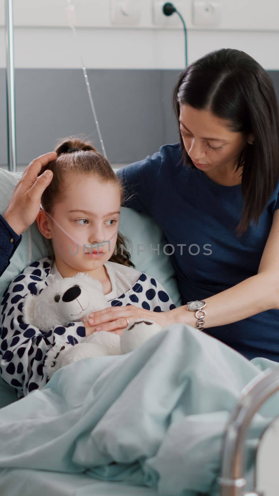 Sick daughter with oxygen nasal tube resting in bed after suffering sickness infection surgery during healthcare examination in hospital ward. Worried parents explaining medication treatment