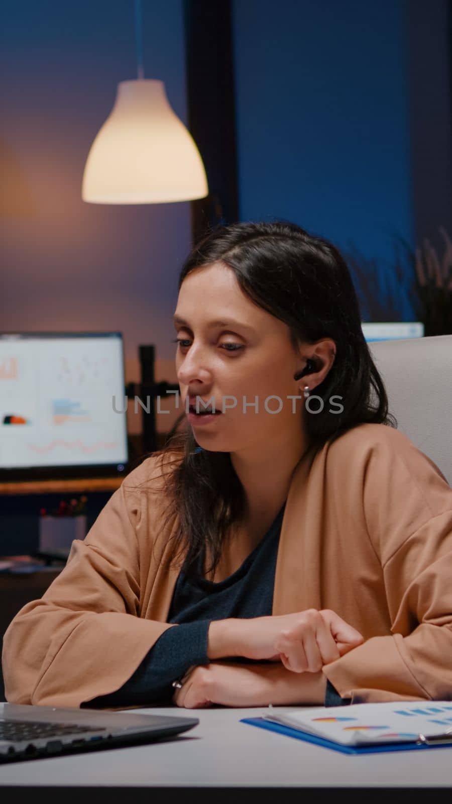 Businesswoman with headphones discussing marketing statistics planning business strategy. Entrepreneur woman talking with her collegues during online videocall conference company meeting in evening