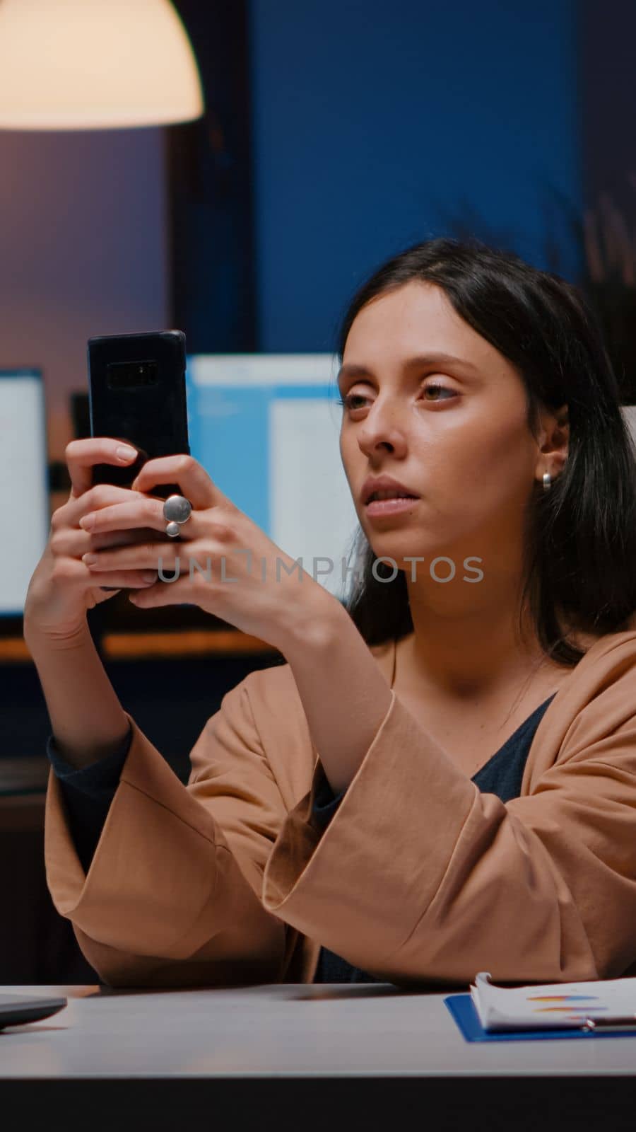 Overworked executive manager holding phone texting marketing ideas analysing social media strategy sitting at desk in business company office. Businesswoman checking online information late at night