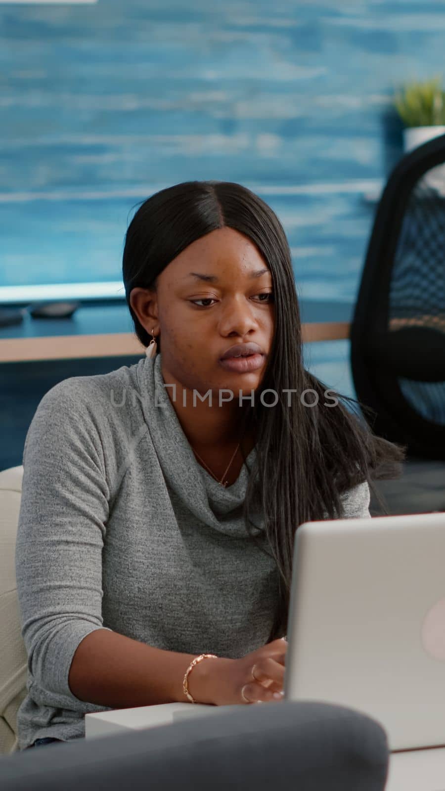 Blogger student with dark skin working from home browsing communication information while drinking coffee sitting on bean bag in living room. African woman working from home at media webinar