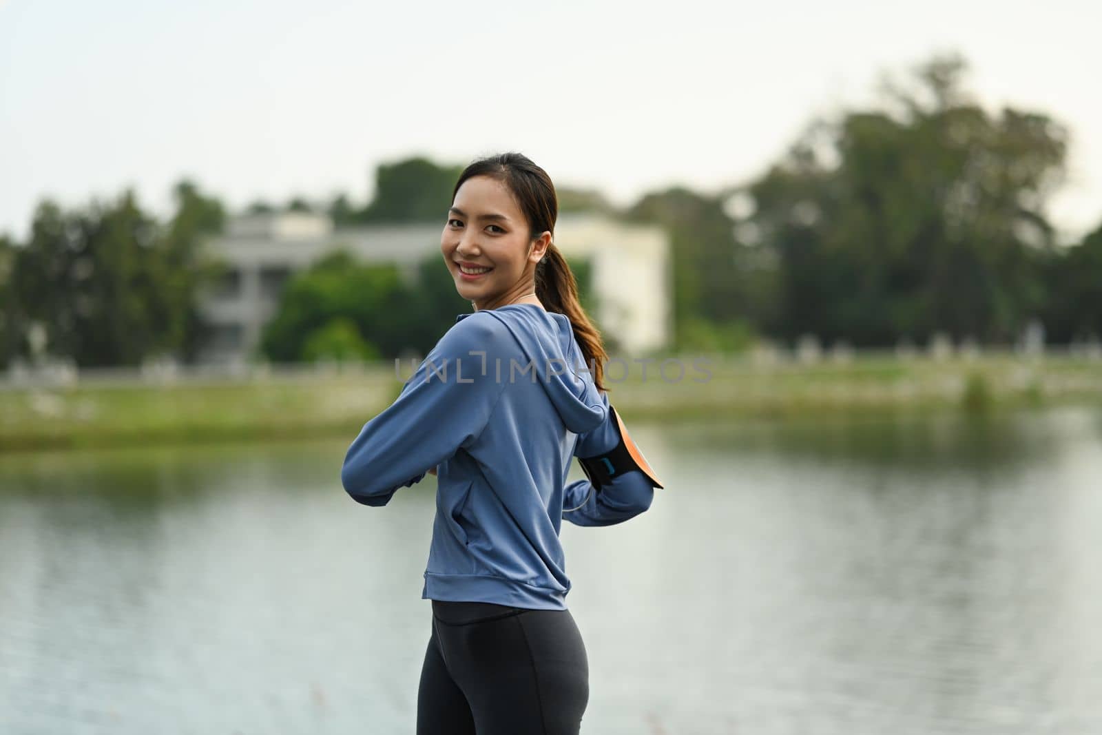 Active sporty female warming up body before workout session at the park in early morning. Healthy lifestyle concept.