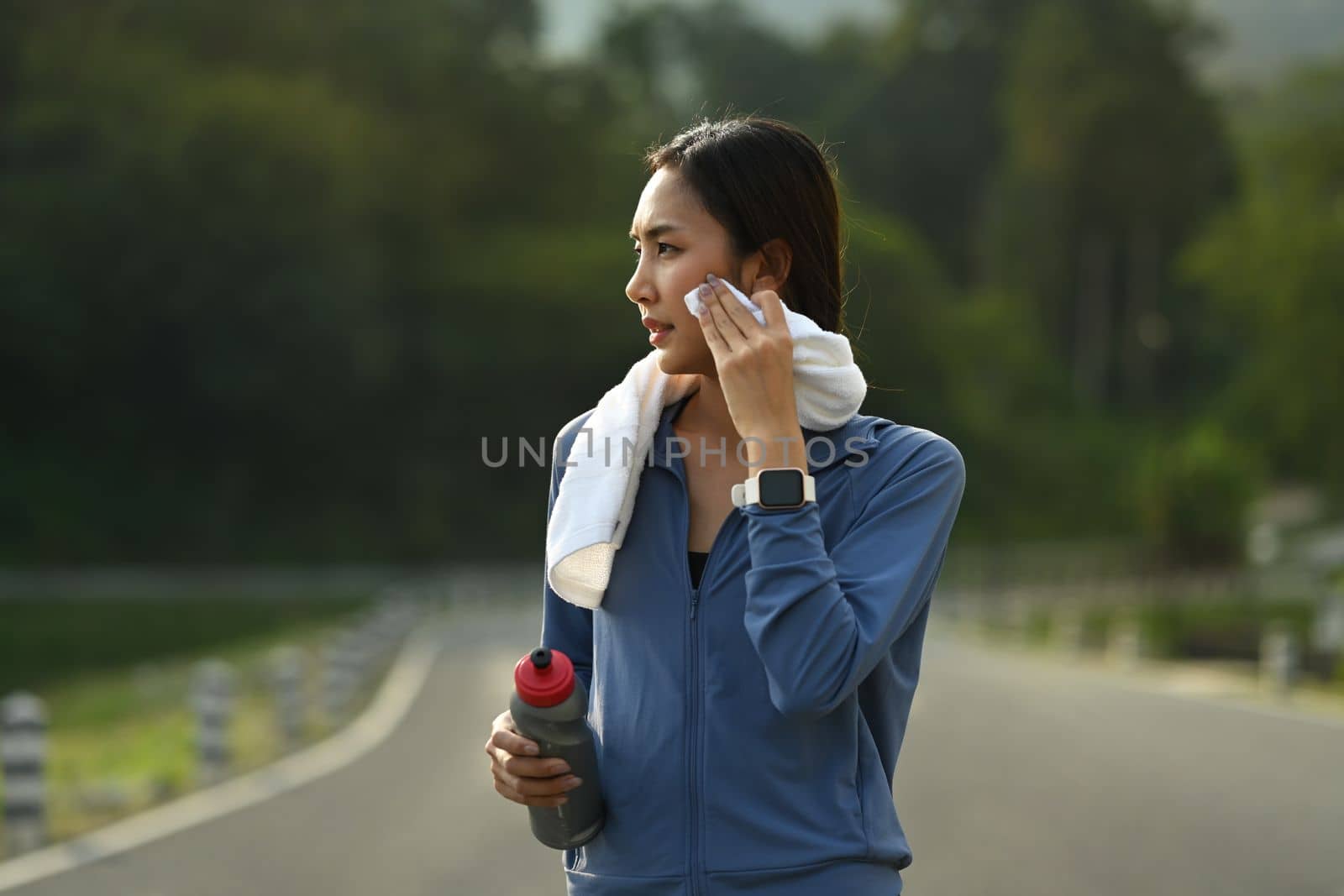 Sportsman wiping sweat towel, taking a break after running outdoors. Healthy lifestyle, workout and wellness concept by prathanchorruangsak