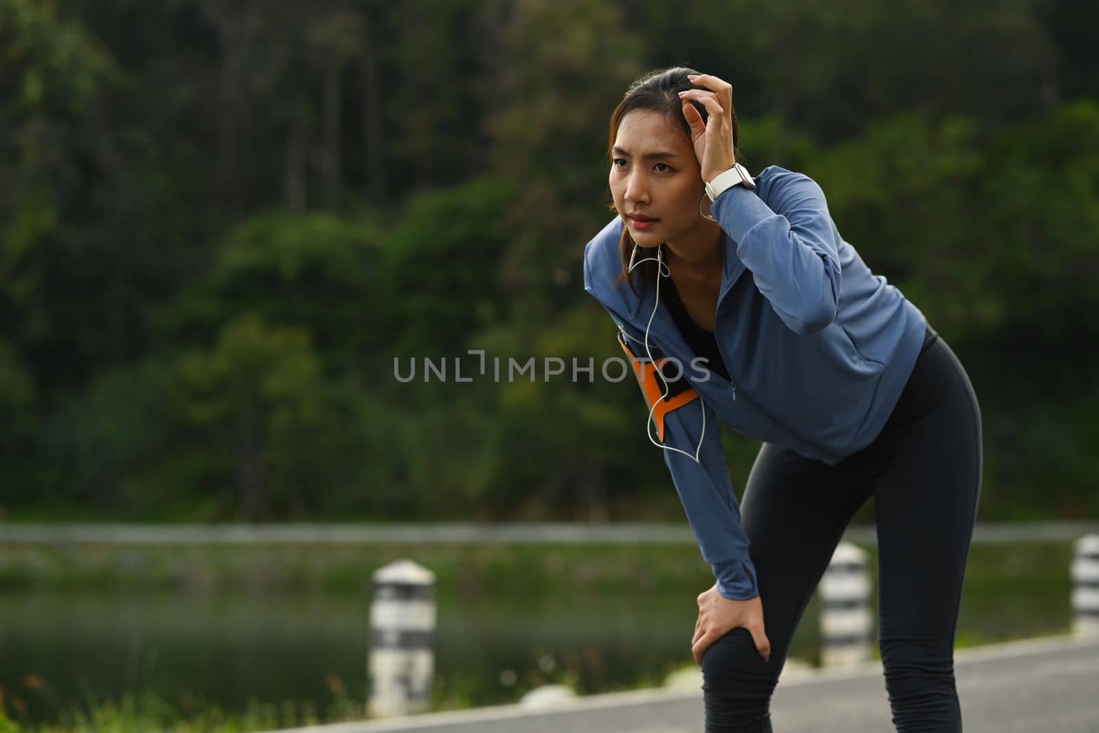 Tired athletic woman in sportswear taking break, resting after running in the park. Healthy lifestyle, workout and wellness concept.