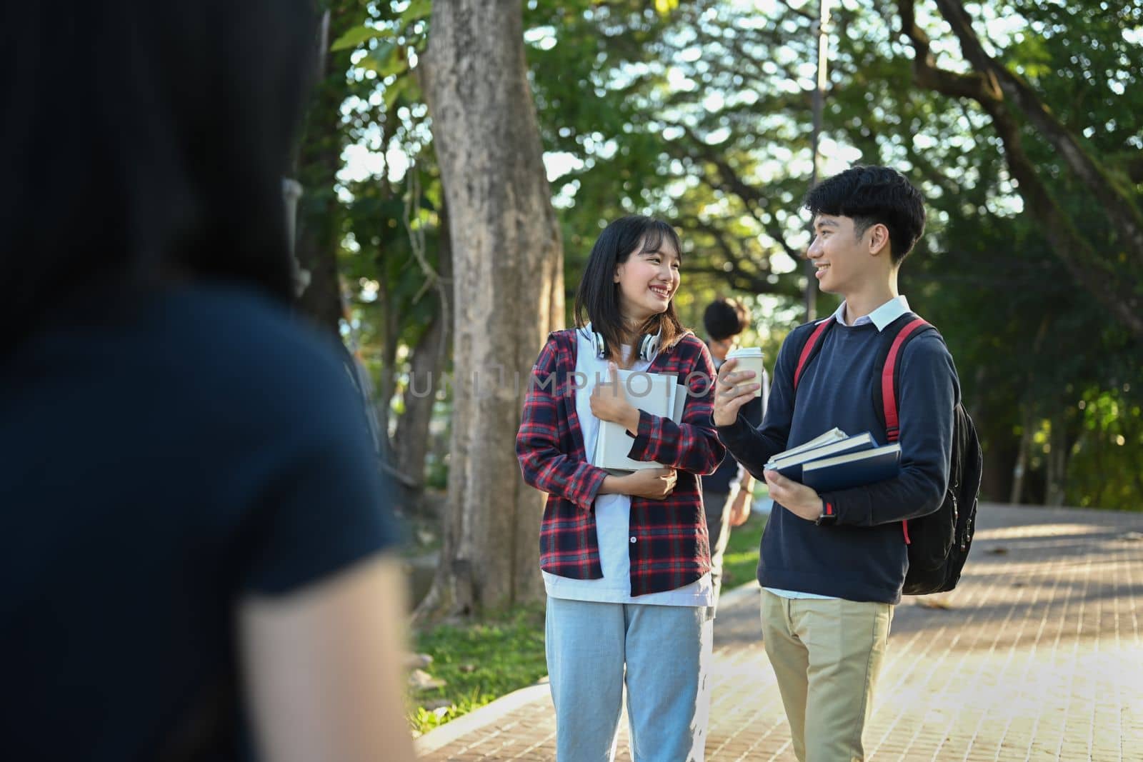 Two happy university student walking in campus, going to lesson and talking to each other. Youth lifestyle and friendship concept.