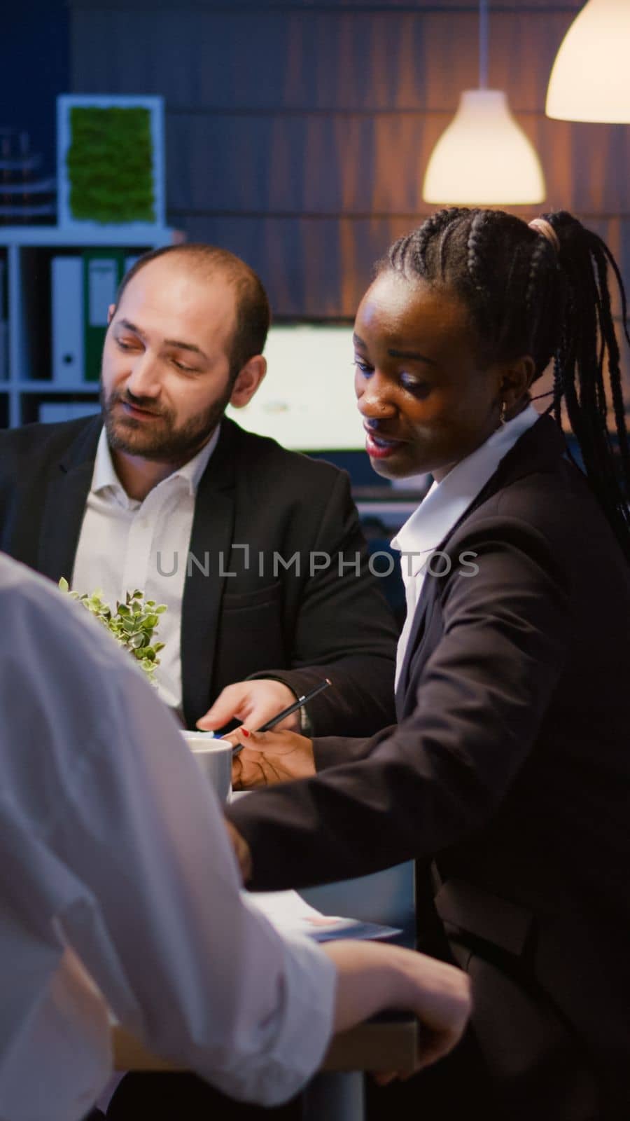 Multi ethnic business team sitting at conference table in office meeting room checking financial graphs presentation overworking at management project. Diverse coworkers brainstorming company ideas