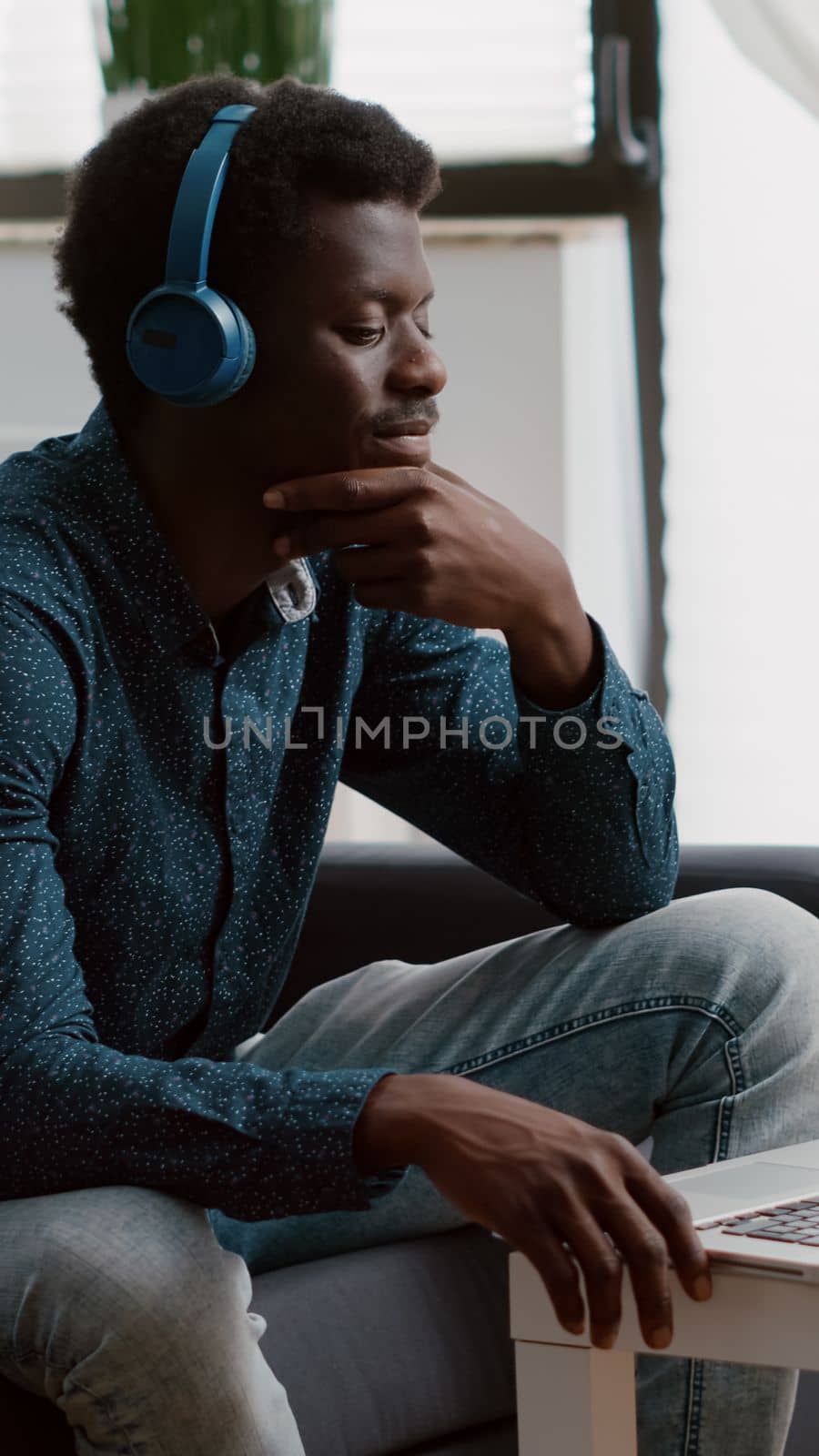Authentic smiling african american man using laptop with headphones on, working from home or freelancer listening webinar or online courses. Taking internet webinar from home office