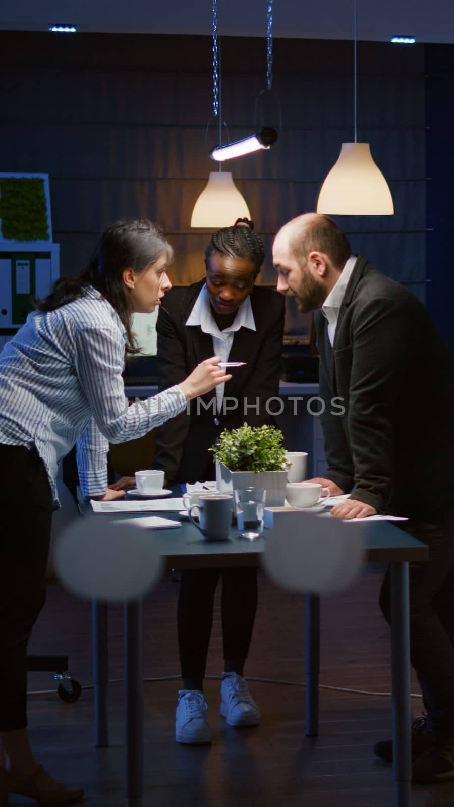 Focused leader woman enter in office meeting room lean on conference table brainstorming business company presentation late at night. Diverse multi ethnic teamwork solving management strategy