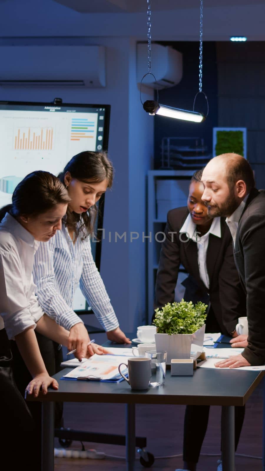 Multi ethnic businesspeople lean on conference table analyzing company strategy ideas by DCStudio