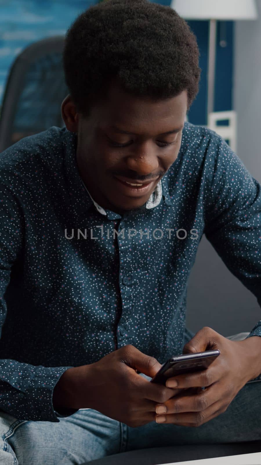 Black guy in his living room using phone to browse social media by DCStudio