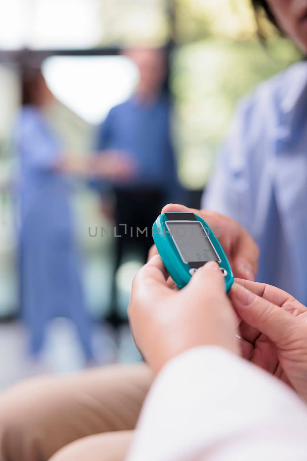 Close up of old doctor measuring insulin and glucose level with glucometer while doing health consultation with diabetic asian patient. Using insturment to check blood sample in hospital reception