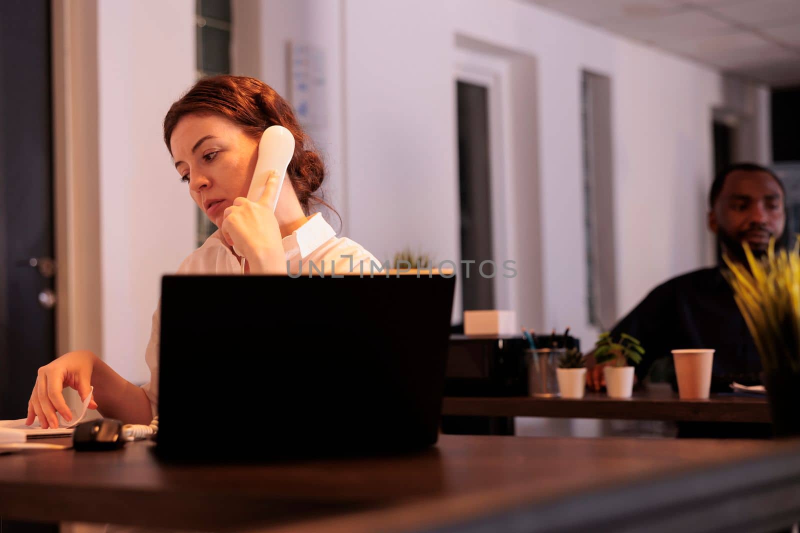 Secretary talking with client on landline phone, discussing report, employee answering customer call. Corporate worker having telephone communication in coworking space at night