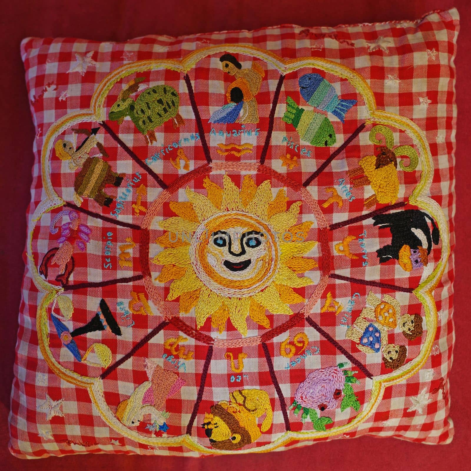 A red and white checkered cushion with embroidered astrological signs. Cute sun in the middle