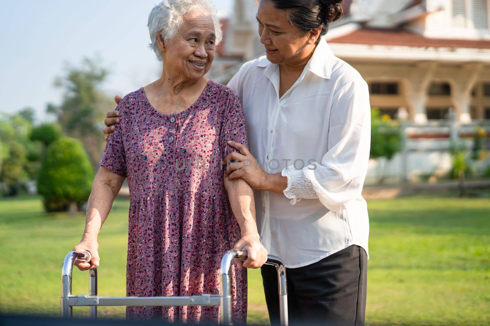 Help and care Asian senior or elderly old lady woman use walker with strong health while walking at park in happy fresh holiday. by pamai