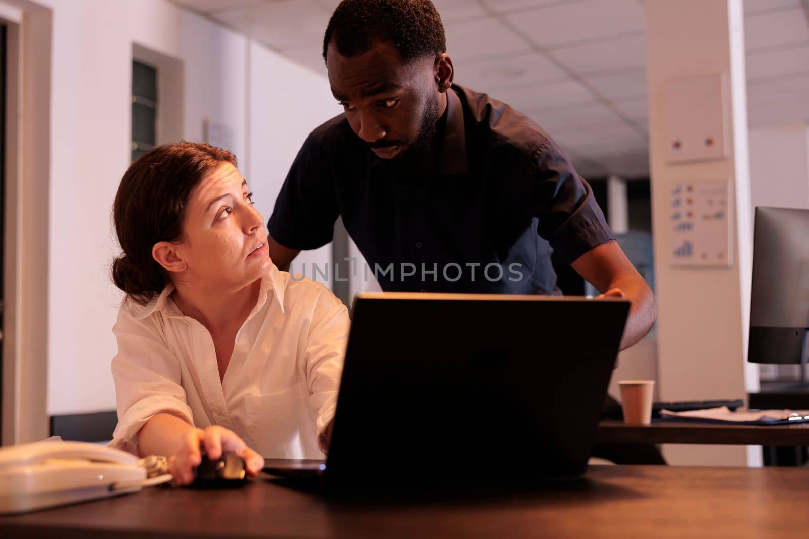 Man helping coworker analyzing report on laptop in office by DCStudio