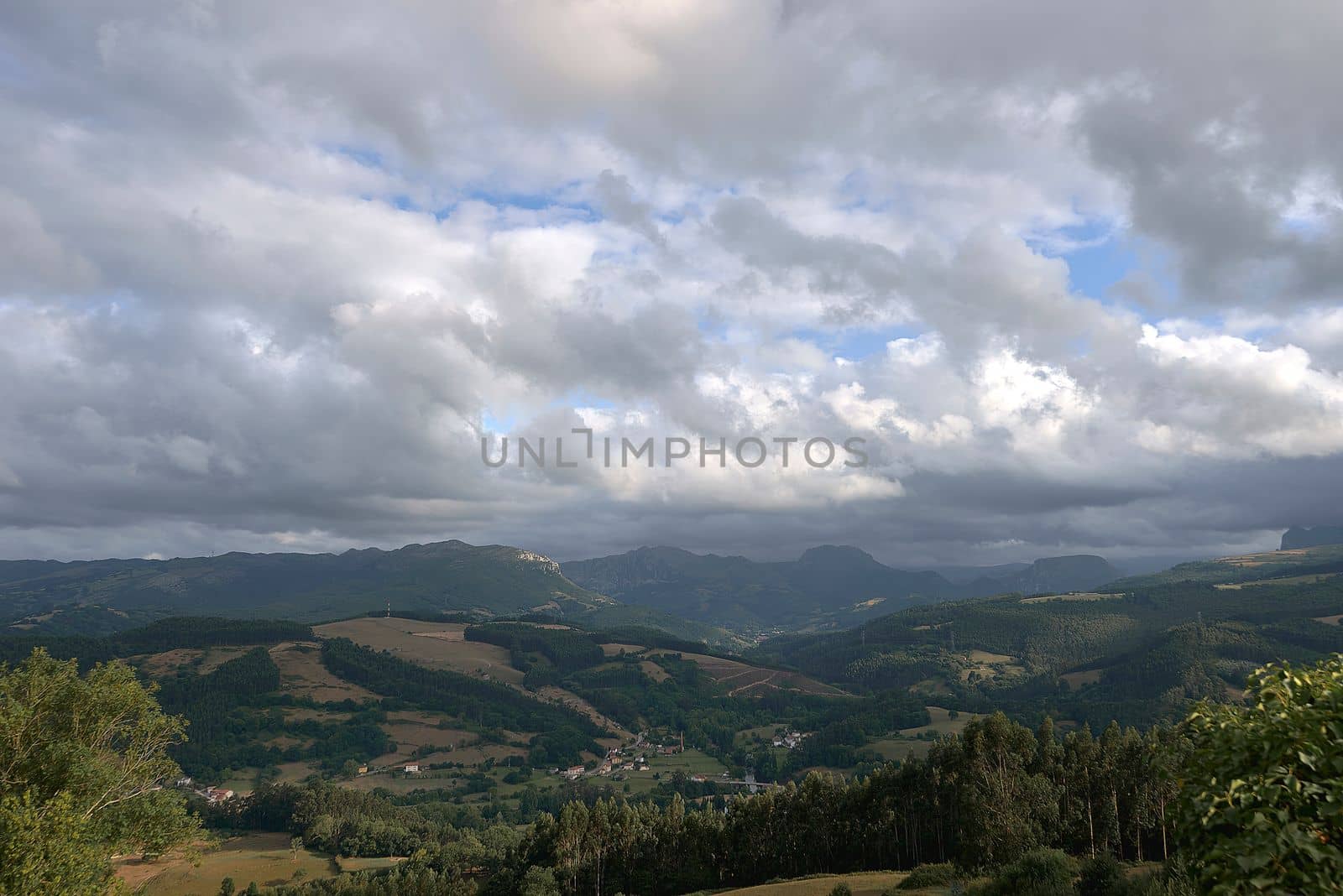 Rustic mountain landscape with cloudy sky.Bien Aparecida, Cantabria, meadows, trees and pastures for animals, rustic houses, sky with storm clouds.