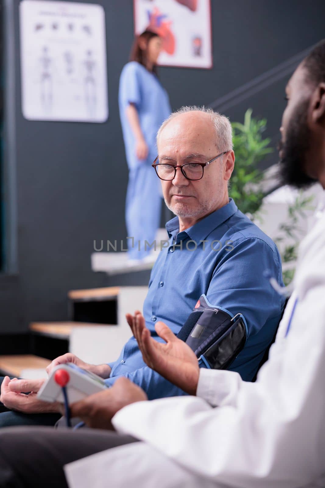 African american cardiologist using tonometer instrument to measure patient pulse pressure and hypertension, doing cardiology examination in hospital waiting room. Old man attending checkup visit.