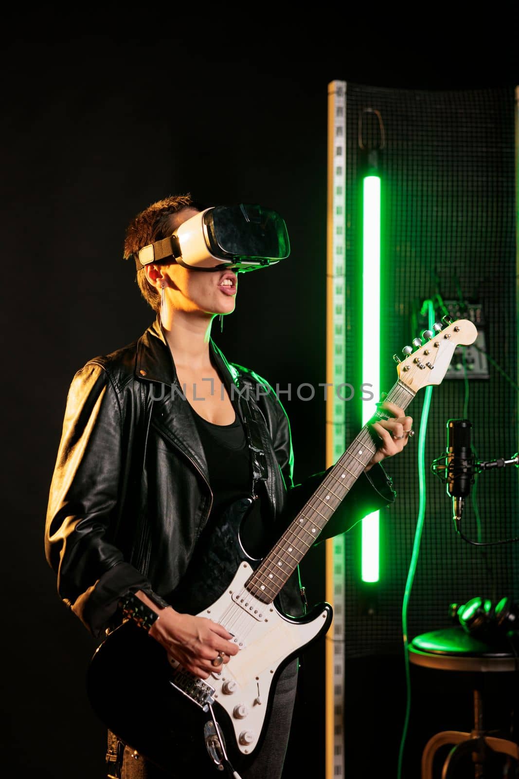 Woman performer playing at electric guitar in sound studio while wearing vr goggles for concert simulation by DCStudio