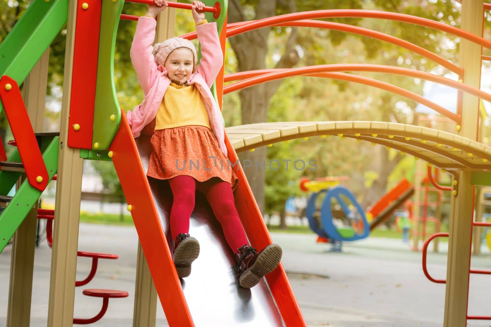 Pretty girl kid playing on playground at autumn day outdoors and enjoying park. Female child happy portrait